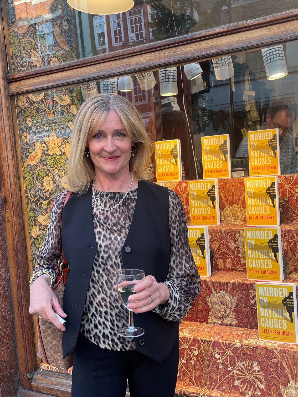 Photo of Helen Erichsen, she is holding a glass of wine outside a bookshop, it is her book launch for the novel "Murder by natural causes"