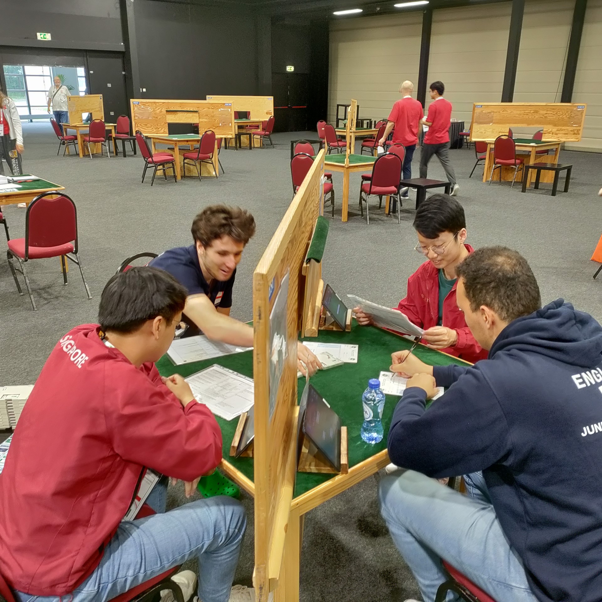 Photo of two of the England youth team and two members of the Singapore youth team at a bridge table with screens
