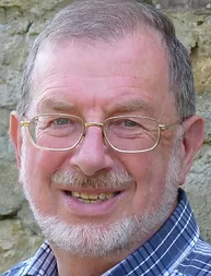 close up photo of an older white man with a short greying beard, he is wearing a blue chequered shirt and glasses